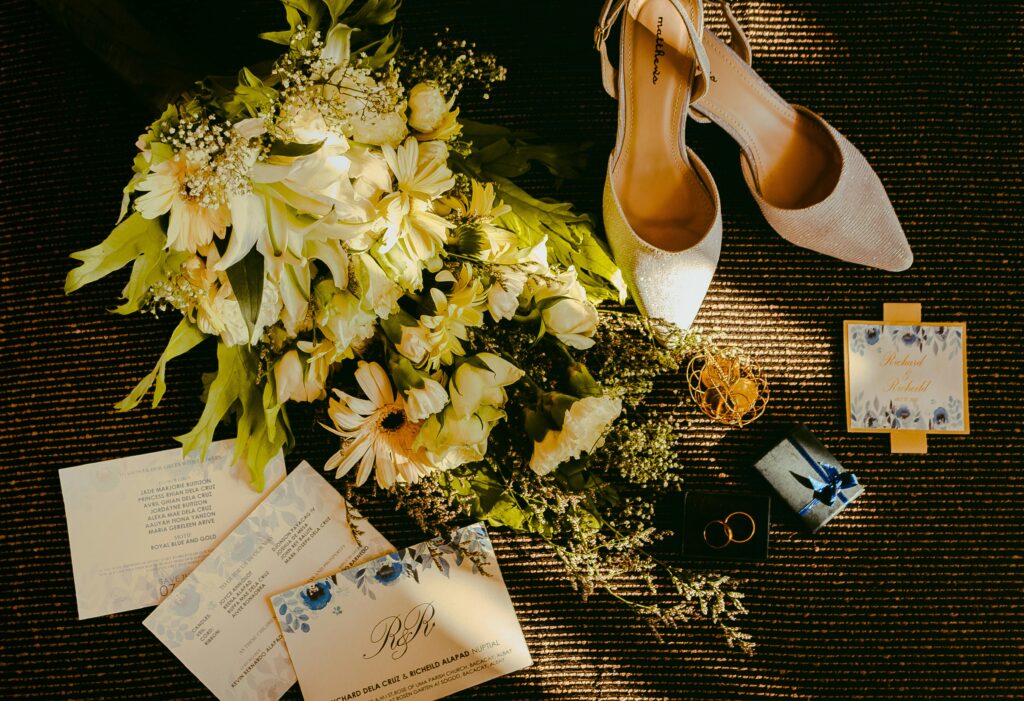 Wedding flat lay featuring shoes, flowers, and invitations with a golden tone.